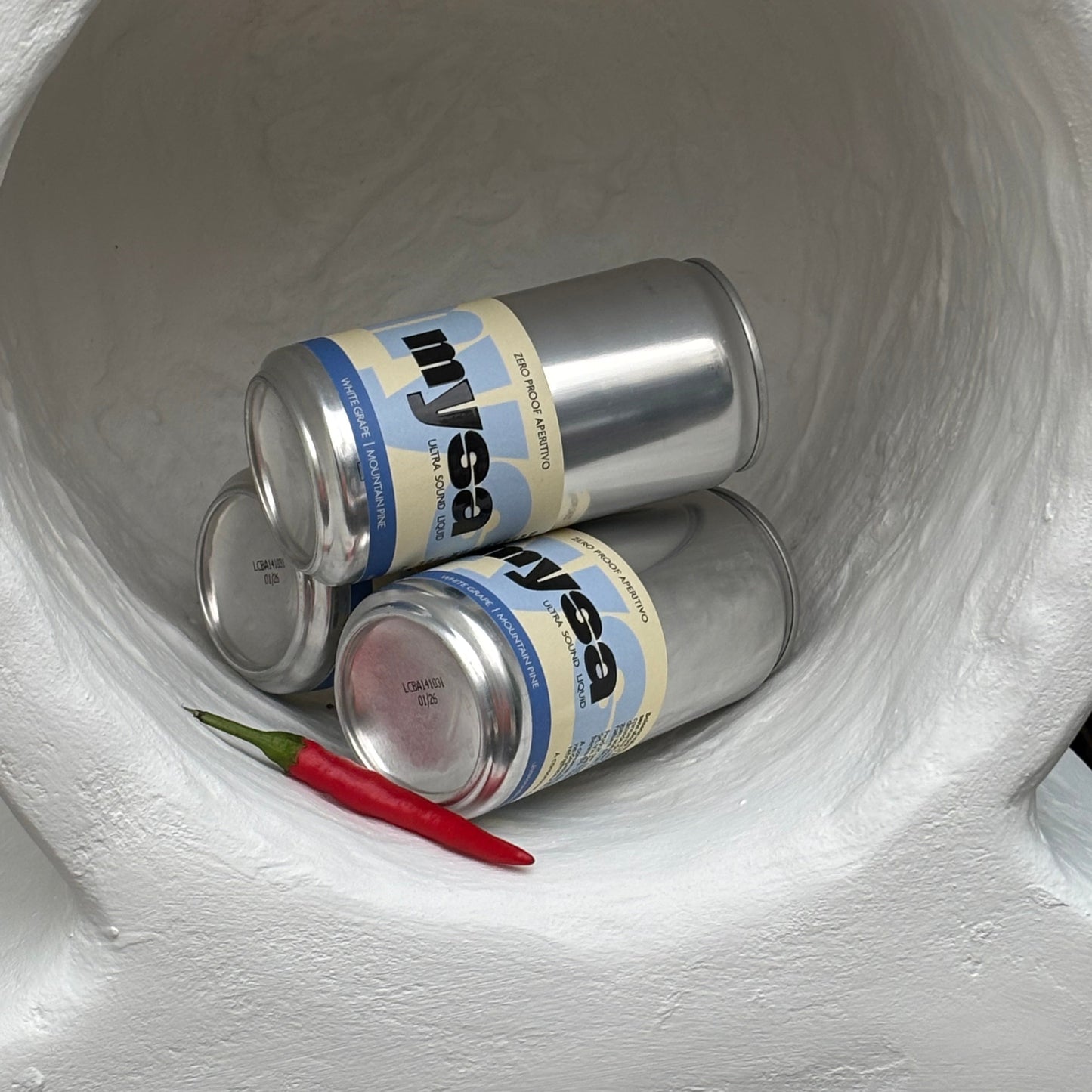 Two cans of Mysa in a white container with a red chili